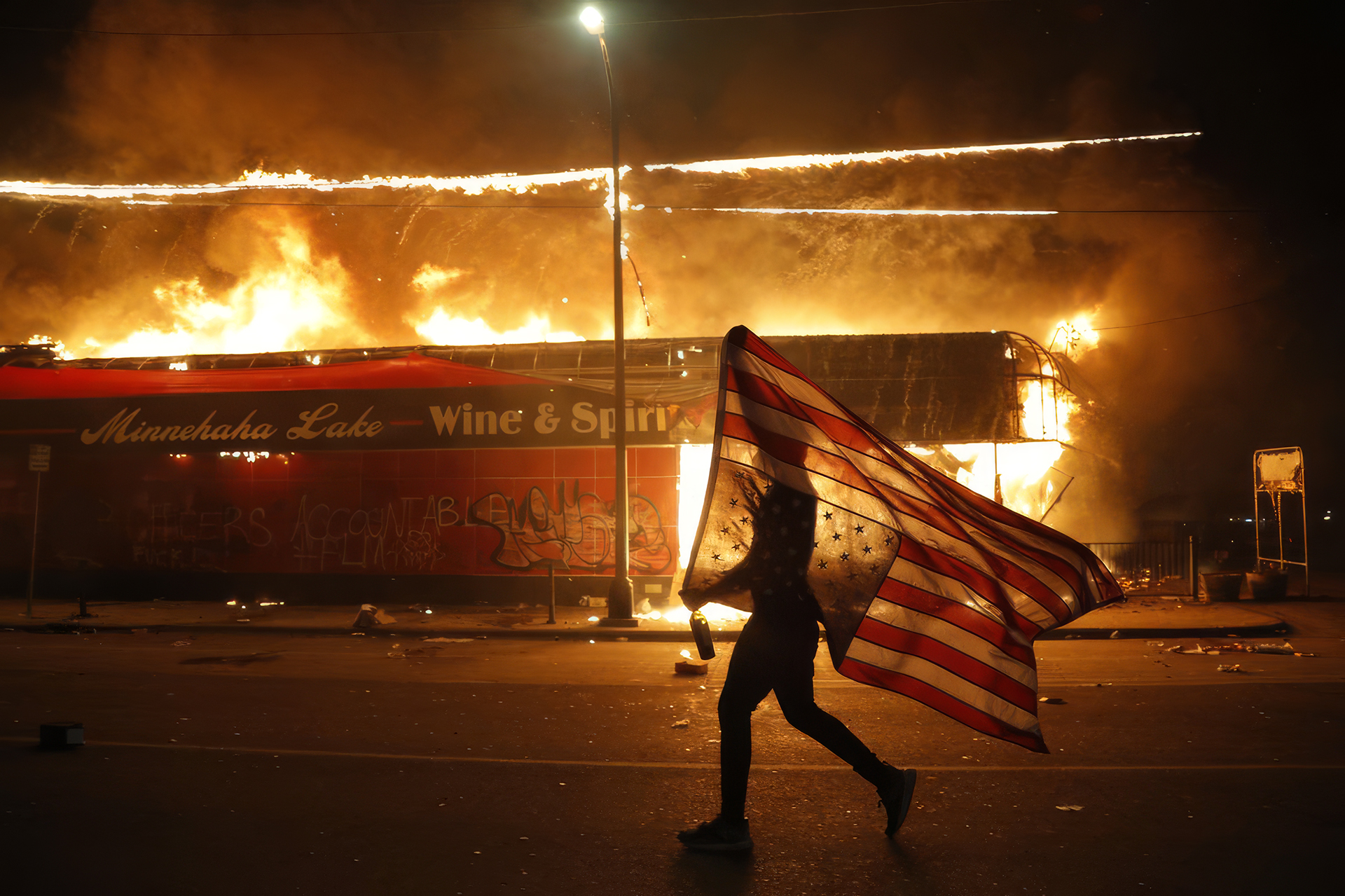 A protester carries an American flag past a burning building during civil unrest