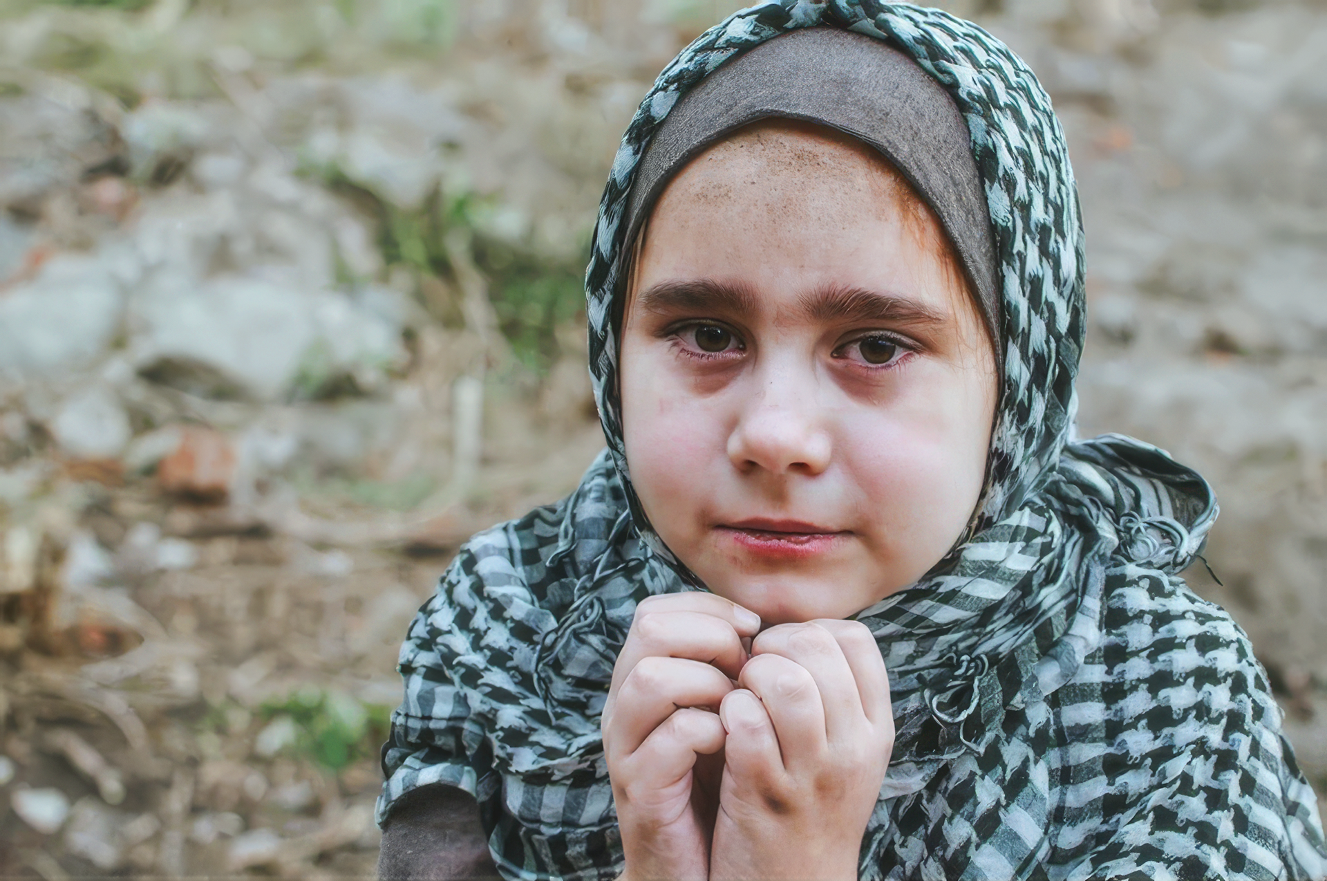 A young refugee girl wearing a patterned scarf, looking directly at the camera