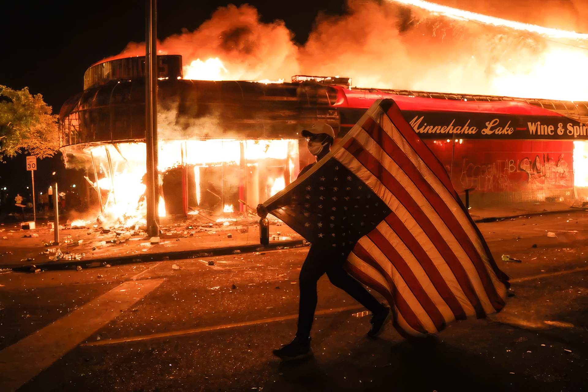 A protester carries an American flag past a burning building