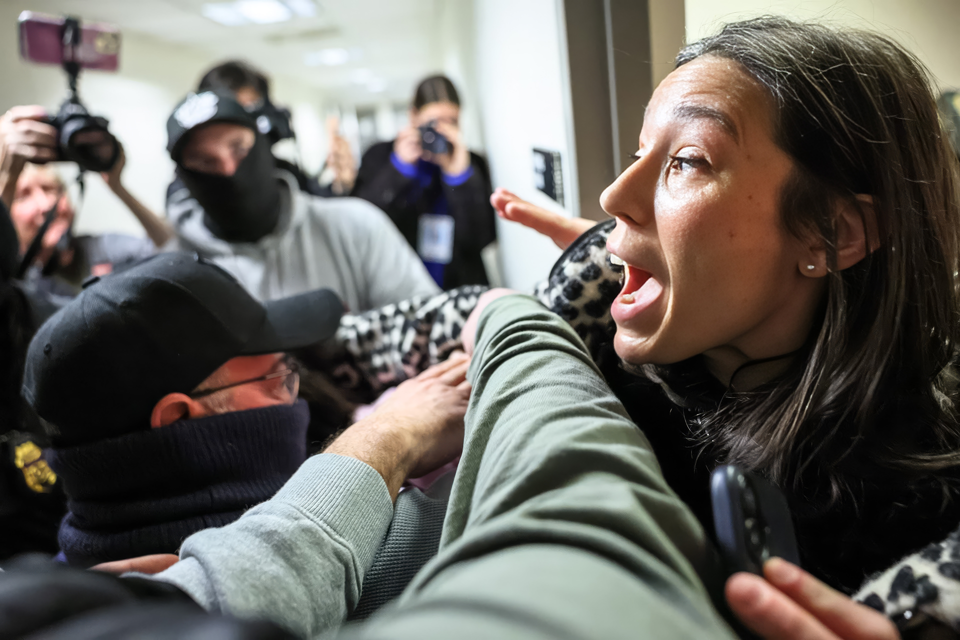 A woman being arrested by masked officers while surrounded by press