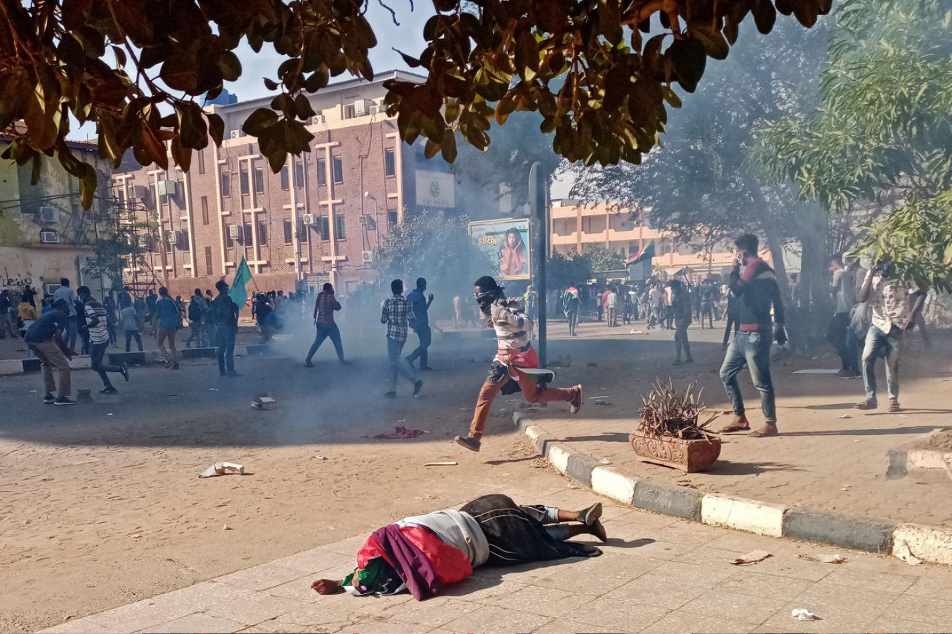 A person lying on the ground during a protest amid smoke and running crowds